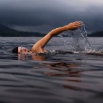 Person swimming in river water under a cloudy sky, image used for Nicholas Fainlight blog on the health benefits of swimming